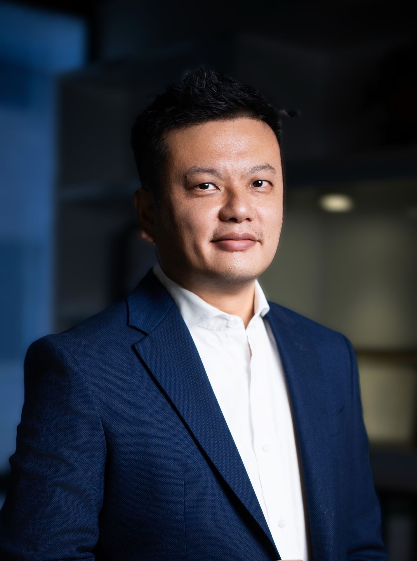 Man in a blue suit and white shirt looking at the camera with a blurred background.