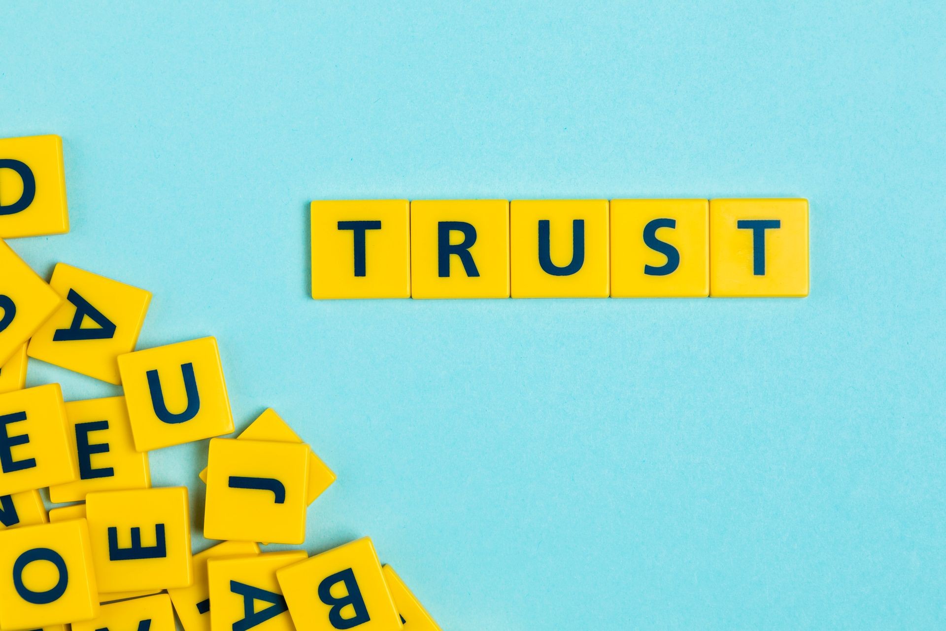 Yellow letter tiles spelling 'TRUST' on a blue background with scattered tiles.