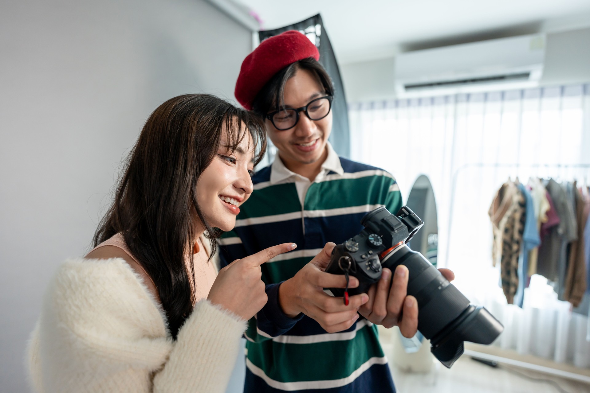 Asian beautiful woman model and cameraman working in photography studio. Attractive professional photographer captures beautiful pictures of young girl with backdrop create images for advertisements.