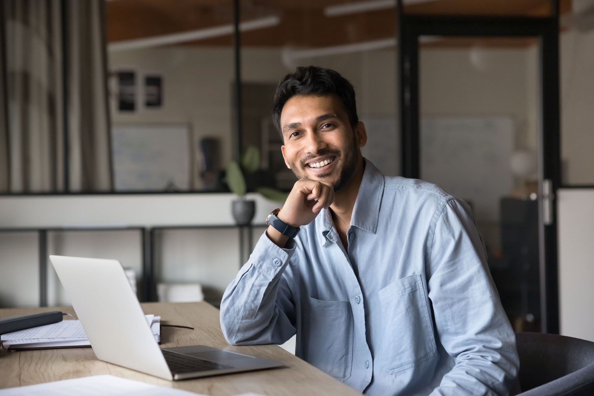 Businessman posing for corporate portrait seated at desk with laptop