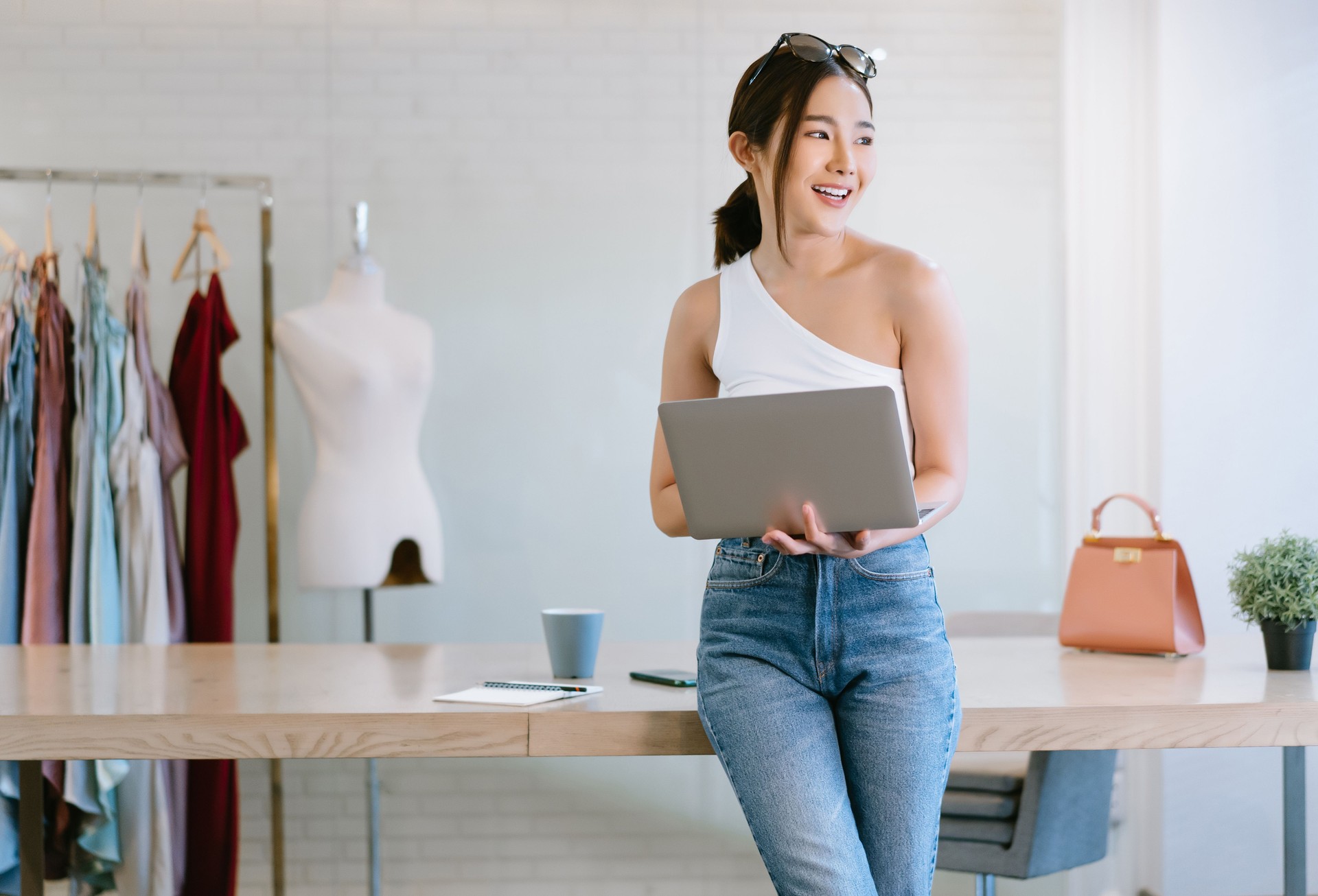Young beautiful Asian Woman fashion designer working small business using laptop computer and look away dream about good future vision in home office. Startup Small business owner, Freelance work.